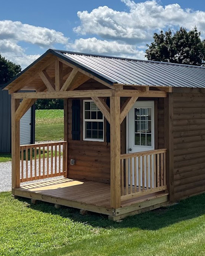 Small log cabin with covered porch, timber posts, and metal roof.